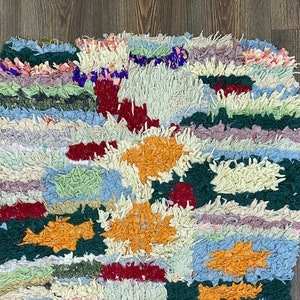 Puede incluir: Una colorida alfombra de trapo hecha a mano con un dise&ntilde;o de patchwork. La alfombra presenta una variedad de colores, incluyendo naranja, rojo, verde, azul y crema. La textura es gruesa y texturizada, con una apariencia peluda. La alfombra es rectangular.