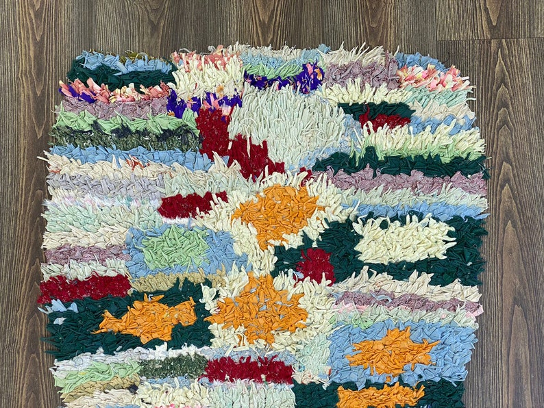 Puede incluir: Una colorida alfombra de trapo hecha a mano con un dise&ntilde;o de patchwork. La alfombra presenta una variedad de colores, incluyendo naranja, rojo, verde, azul y crema. La textura es gruesa y texturizada, con una apariencia peluda. La alfombra es rectangular.