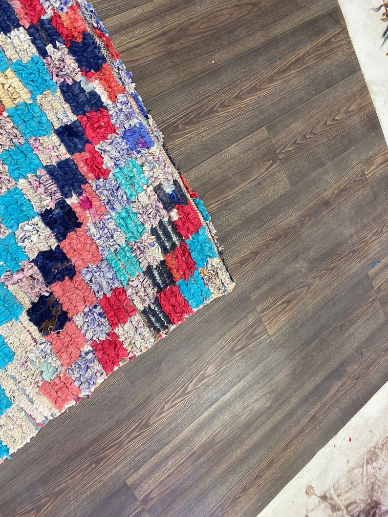 May include: A colorful, handwoven rug with a variety of blues, reds, and pinks. The rug is made of recycled materials and has a unique, textured look.