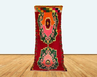 May include: A vibrant, rectangular rug with a red background and colorful geometric patterns. The rug features orange, pink, green, and yellow accents, creating a striking visual contrast. The rug's design includes symmetrical floral-like motifs.