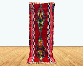 May include: A long, narrow red rug with a colorful geometric pattern. The rug has a fringe on both ends.