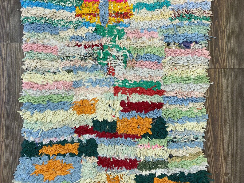 Puede incluir: Una alfombra colorida y texturizada con un dise&ntilde;o de patchwork. La alfombra presenta una variedad de colores, incluyendo azul, verde, rosa, amarillo y naranja. La alfombra est&aacute; hecha de tiras de tela y tiene un aspecto hecho a mano.
