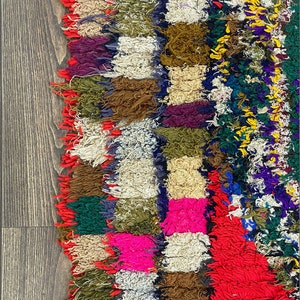Pu&ograve; includere: Un tappeto colorato tessuto a mano con un design a patchwork. Il tappeto &egrave; fatto di vari colori, tra cui rosso, rosa, verde, blu e giallo. Il tappeto ha un bordo sfrangiato e una superficie testurizzata.