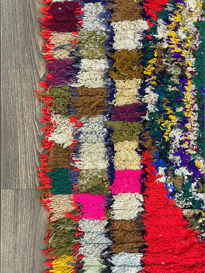 Pu&ograve; includere: Un tappeto colorato tessuto a mano con un design a patchwork. Il tappeto &egrave; fatto di vari colori, tra cui rosso, rosa, verde, blu e giallo. Il tappeto ha un bordo sfrangiato e una superficie testurizzata.