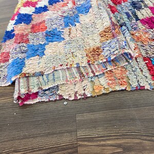 May include: A colorful, hand-woven rug with a patchwork design. The rug is made of various shades of blue, red, pink, and white.