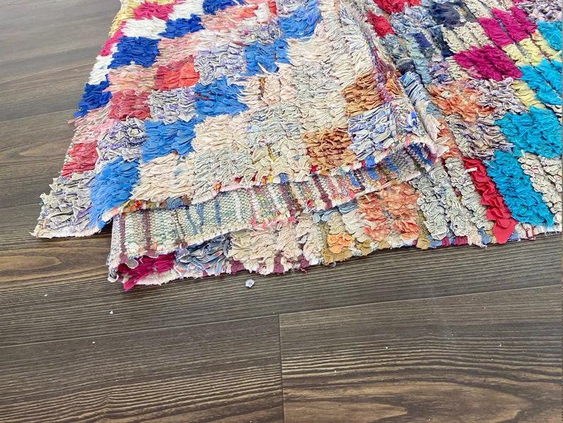 May include: A colorful, hand-woven rug with a patchwork design. The rug is made of various shades of blue, red, pink, and white.