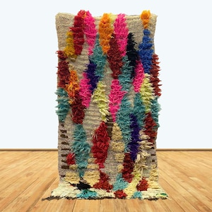 May include: A colourful Moroccan rug with a shaggy texture. The rug features a variety of colours, including pink, blue, yellow, and red. The rug is made of wool and is hand-woven.