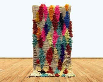 May include: A colorful Moroccan rug with a shaggy texture. The rug features a variety of colors, including pink, blue, yellow, and red. The rug is made of wool and is hand-woven.