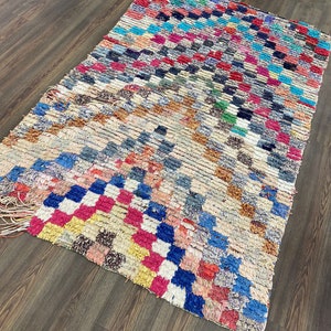May include: A colorful Moroccan rug with a geometric pattern in shades of blue, red, pink, yellow, and white. The rug has a distressed, vintage look and is made of wool.