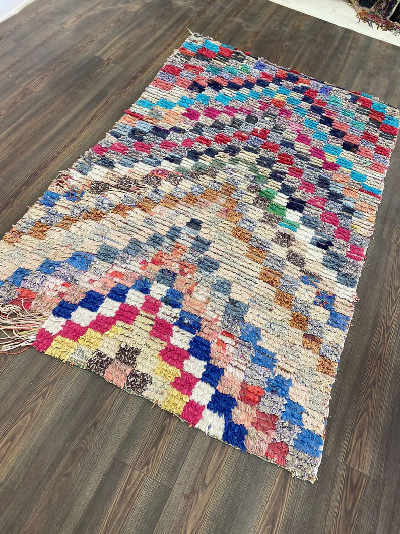 May include: A colorful Moroccan rug with a geometric pattern in shades of blue, red, pink, yellow, and white. The rug has a distressed, vintage look and is made of wool.