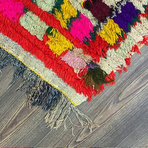 Pu&ograve; includere: Un tappeto colorato tessuto a mano con un bordo a frangia. Il tappeto &egrave; fatto di lana e ha una variet&agrave; di colori, tra cui rosso, giallo, verde, blu e rosa.