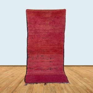 May include: A long, narrow, red rug with a dark border and fringe. The rug is lying flat on a wooden floor.