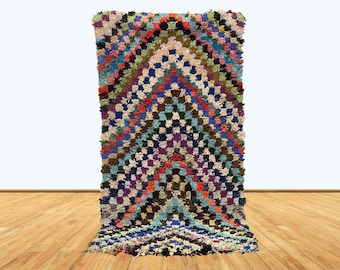 May include: A colorful Moroccan rug with a geometric pattern in shades of blue, green, red, and white. The rug has a thick, fluffy texture and is made of wool.