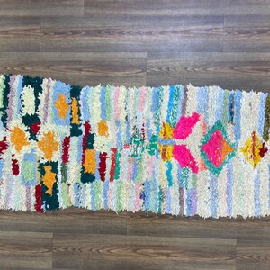 Puede incluir: Una alfombra rectangular y colorida con un dise&ntilde;o de patchwork. La alfombra presenta rayas verticales en varios colores pastel, con patrones geom&eacute;tricos en naranja, rosa y verde. La alfombra est&aacute; hecha de un material texturizado.
