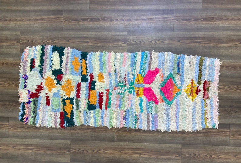 Puede incluir: Una alfombra rectangular y colorida con un dise&ntilde;o de patchwork. La alfombra presenta rayas verticales en varios colores pastel, con patrones geom&eacute;tricos en naranja, rosa y verde. La alfombra est&aacute; hecha de un material texturizado.