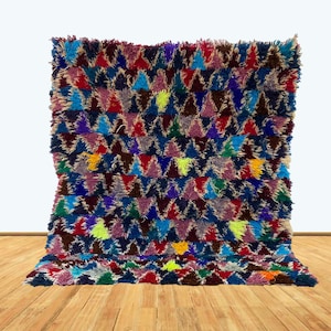 May include: A colorful Moroccan rug with a geometric pattern of triangles in shades of blue, red, purple, green, and yellow. The rug has a shaggy texture and is made of wool.