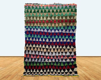 May include: A colorful Moroccan rug with a geometric pattern of triangles in shades of red, green, blue, black, and white. The rug is woven with a thick, textured pile.