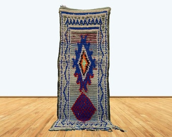 Puede incluir: Una alfombra larga y estrecha con un patrón geométrico azul, rojo y blanco. La alfombra tiene flecos en la parte inferior y está hecha de lana.