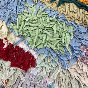 Puede incluir: Primer plano de un textil con dise&ntilde;o de patchwork. La tela presenta una variedad de colores, incluyendo azul claro, verde, rojo y beige. La textura parece estar hecha de tiras de tela, creando un efecto en capas. La est&eacute;tica general es r&uacute;stica y hecha a mano.