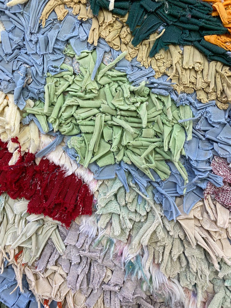 Puede incluir: Primer plano de un textil con dise&ntilde;o de patchwork. La tela presenta una variedad de colores, incluyendo azul claro, verde, rojo y beige. La textura parece estar hecha de tiras de tela, creando un efecto en capas. La est&eacute;tica general es r&uacute;stica y hecha a mano.