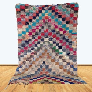 May include: A colorful Moroccan rug with a geometric pattern in shades of red, blue, green, and white. The rug is made of wool and has a hand-woven texture.