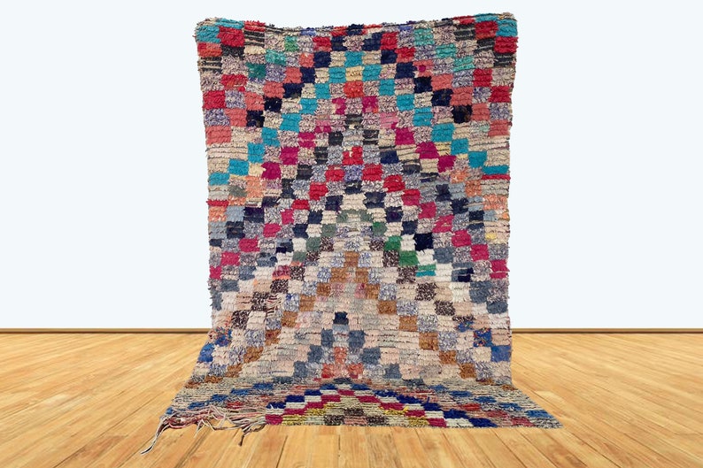May include: A colorful Moroccan rug with a geometric pattern in shades of red, blue, green, and white. The rug is made of wool and has a hand-woven texture.