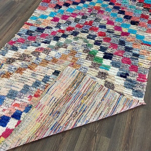 May include: A colorful, handwoven rug with a checkered pattern in shades of blue, red, green, and white. The rug is made of wool and has a frayed edge.