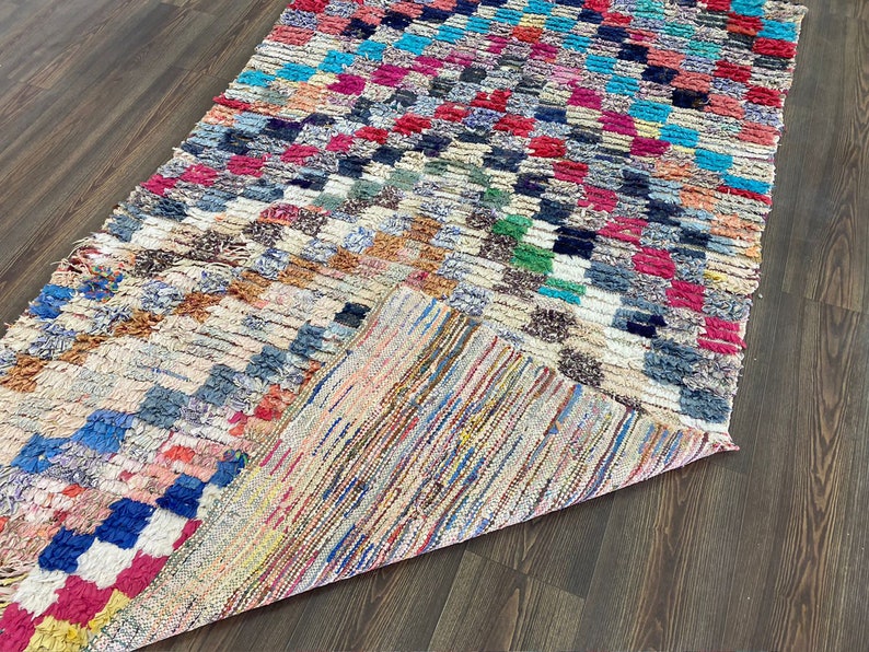 May include: A colorful, handwoven rug with a checkered pattern in shades of blue, red, green, and white. The rug is made of wool and has a frayed edge.