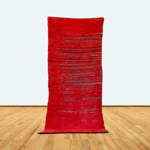 May include: A long, red rug with a woven pattern. The rug is on a wooden floor.