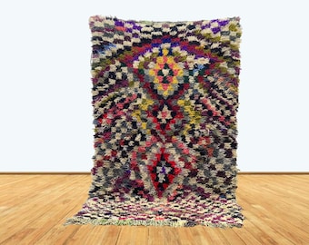 May include: A colorful Moroccan rug with a geometric pattern in shades of red, pink, purple, blue, green, yellow, and white. The rug has a thick, fluffy texture and is made of wool.