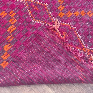 Pode incluir: Um tapete vibrante magenta e laranja com um design geom&eacute;trico. O tapete apresenta um padr&atilde;o repetitivo de formas laranja e cinza sobre um fundo magenta. A borda do tapete &eacute; vis&iacute;vel, mostrando a parte inferior.
