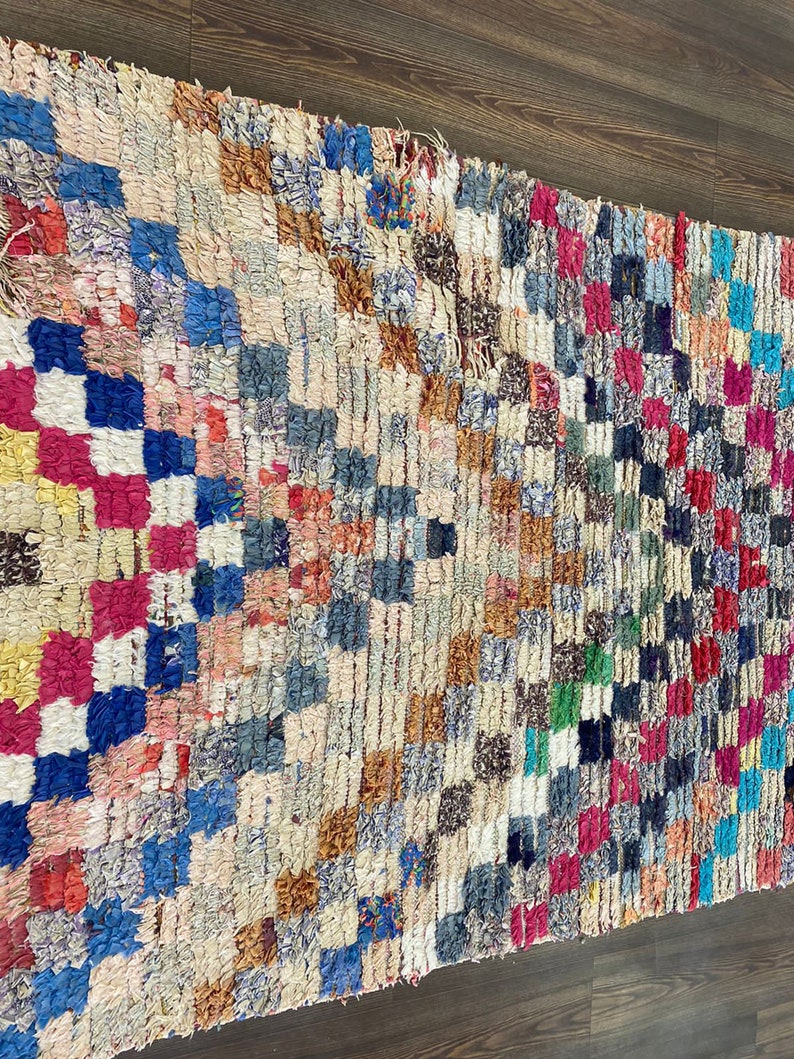 May include: A colorful Moroccan rug with a geometric pattern in shades of blue, red, pink, yellow, and brown. The rug is made of wool and has a hand-woven texture.