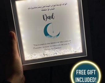 May include: A white framed light-up sign with a crescent moon and clouds design. The sign says "Dad" and includes an Arabic quote and the text "The father is the middle of the gates of paradise, so keep to this gate or lose it. (Sunan At-Tirmizi)".