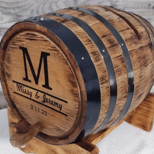 May include: A wooden barrel with black metal bands and a personalized inscription. The inscription reads "M Missy & Jeremy 2.11.23".