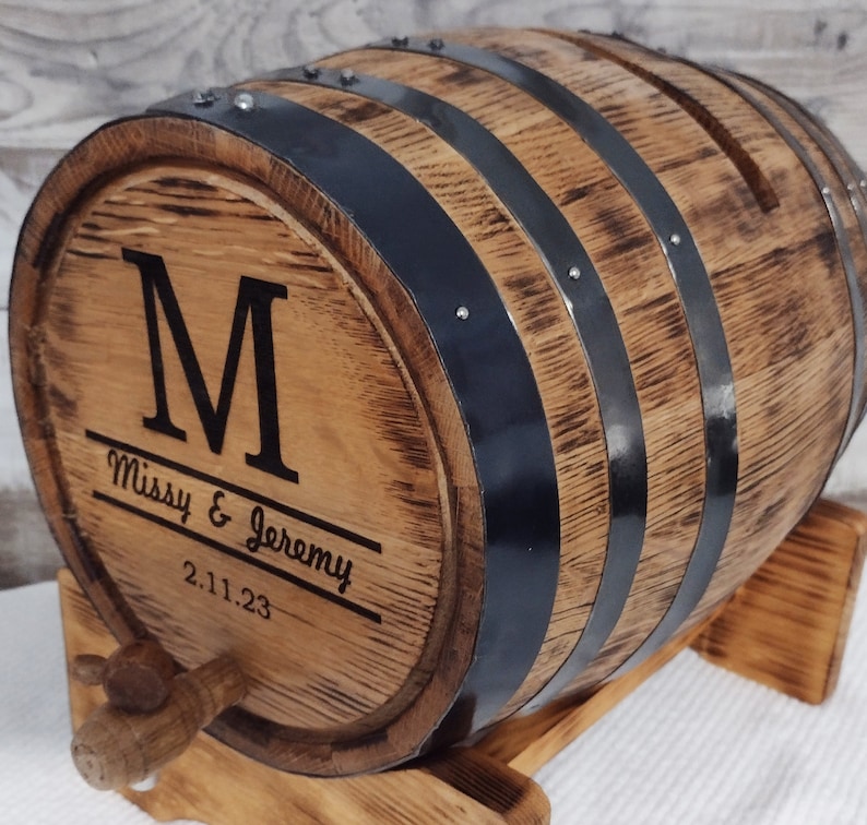 May include: A wooden barrel with black metal bands and a personalized inscription. The inscription reads "M Missy & Jeremy 2.11.23".