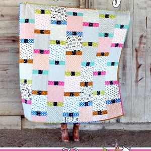 May include: A colorful quilt with a patchwork design featuring squares of various colors and patterns. The quilt is titled "Flutterby" and is made by Running Doe Quilts for Villa Rosa Designs.