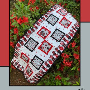 May include: A handmade quilt with a tea-themed design. The quilt features squares with teacups, spoons, and teapots in red, black, and gray on a white background. The words "Tea for 2" are at the top. Designed by Molly Cook for Villa Rosa Designs.