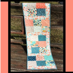 May include: A colorful patchwork quilt table runner with a floral pattern, teal, pink, and white squares. The runner is on a wooden bench. The text "Macarons" is at the top of the image. The text "Tricia Lynn Maloney Orphan Quilt Designs For Villa Rosa Designs" is at the bottom of the image.