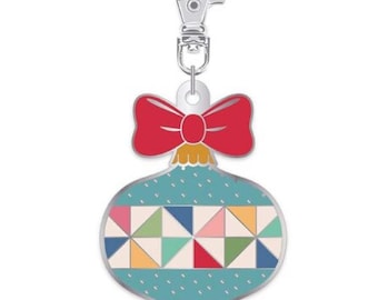 May include: Ornament-shaped keychain with a red bow and a silver clasp. The ornament has a teal background with a geometric pattern of colorful triangles. A festive accessory.