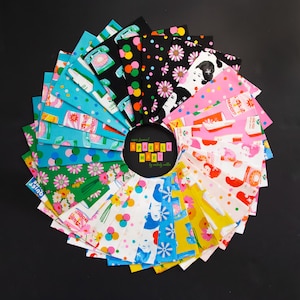 Op de afbeelding: Een cirkelvormige opstelling van stofstalen met diverse patronen, waaronder retro telefoons, bloemmotieven, stippen en gestileerde gezichten in levendige kleuren. Een centraal zwart label toont de tekst "now famous! SPARKLE MART by melody miller".