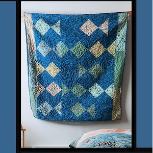 May include: A blue quilt with a diamond pattern in shades of blue, green, and tan hangs on a wall. The quilt is labeled "Go Fish" at the top. The quilt is a design by Tricia Lynn Maloney for Villa Rosa Designs.