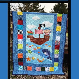 May include: A handmade quilt with a pirate ship design. The quilt features a blue background with a pirate ship, fish, and a shark. The word "Charlie" is at the top. The quilt is bordered with colorful squares.