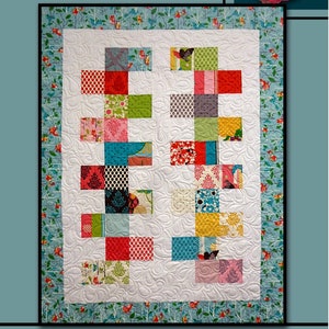 May include: A quilt pattern called "Parade" by Villa Rosa Designs. The quilt is made of colorful patchwork squares in a variety of patterns and colors, including red, green, blue, yellow, and pink. The quilt is surrounded by a blue and white border with a floral pattern.