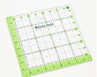 Könnte beinhalten: Ein klarer, quadratischer Quilt-Lineal mit grünen Kanten und Markierungen. Das Lineal hat ein Rastermuster und den Text "Cute Cuts". Das Lineal misst etwa 10 cm pro Seite, mit Messungen in Zoll.