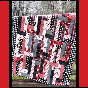 May include: A quilt pattern called "Bear Hugs" designed by Tricia Lynn Maloney for Orphan Quilt Designs and Villa Rosa Designs. The quilt features a patchwork design with red, black, white, and gray fabric. The quilt is displayed on a wooden bench.