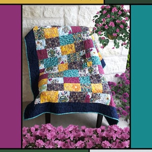 May include: A quilt pattern called "Jericho Walls" by Kate Griffin for Villa Rosa Designs. The quilt is made of colorful fabric squares in shades of blue, green, yellow, and red. The quilt is displayed on a chair in front of a brick wall.
