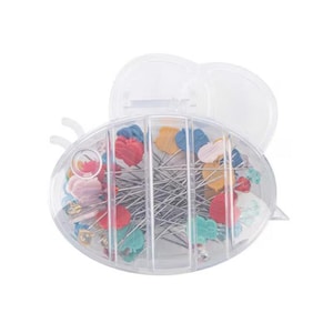 Op de afbeelding: Een doorzichtige, bijvormige container gevuld met spelden. De spelden hebben kleurrijke, decoratieve koppen in verschillende vormen en kleuren, waaronder harten en bladeren. De container is open en onthult de spelden binnenin.