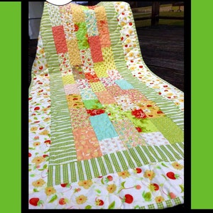 May include: A colorful quilt with the word "Flora" above it. The quilt features a patchwork design with various floral patterns in shades of red, yellow, green, and peach. The quilt is displayed on a chair.
