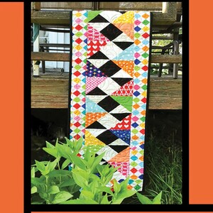 May include: A colorful quilt pattern with black and white triangles and a colorful border. The quilt is titled "Steppin' Up" and is by Tricia Lynn Maloney, Orphan Quilt Designs for Villa Rosa Designs.
