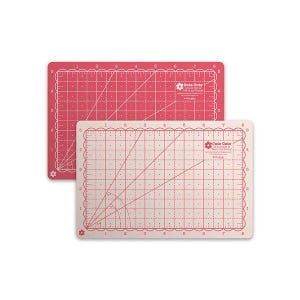 May include: Two rectangular cutting mats. One is light pink, the other is a darker pink. Both have grid lines, angle guides, and scalloped edges. The text "Cute Cute" is visible on both mats. These mats are ideal for sewing and crafting.